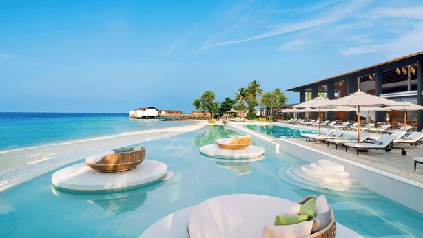 A pool area with lounge chairs and umbrellas, a beach view, and a building with a modern design. - The Westin Maldives Miriandhoo Resort (Miriandhoo Island)