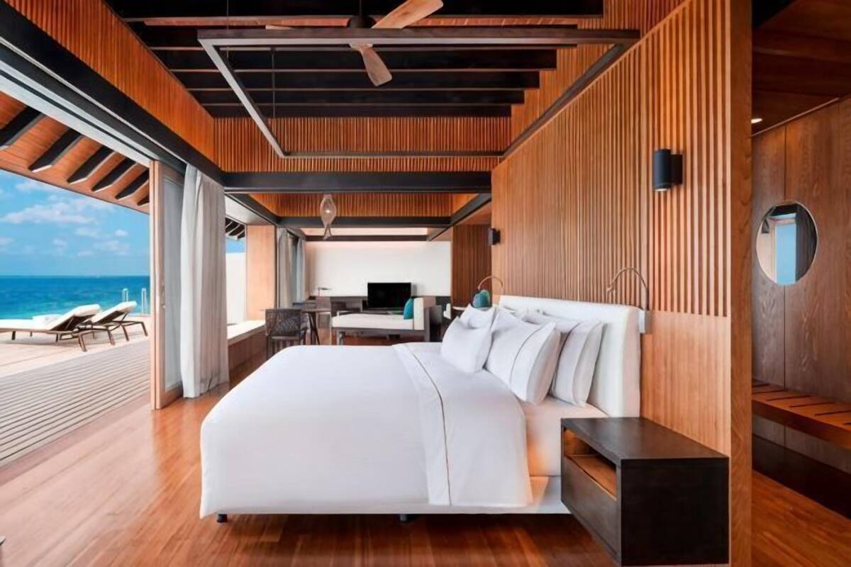 A modern bedroom with a large bed, a desk, and a view of the ocean.