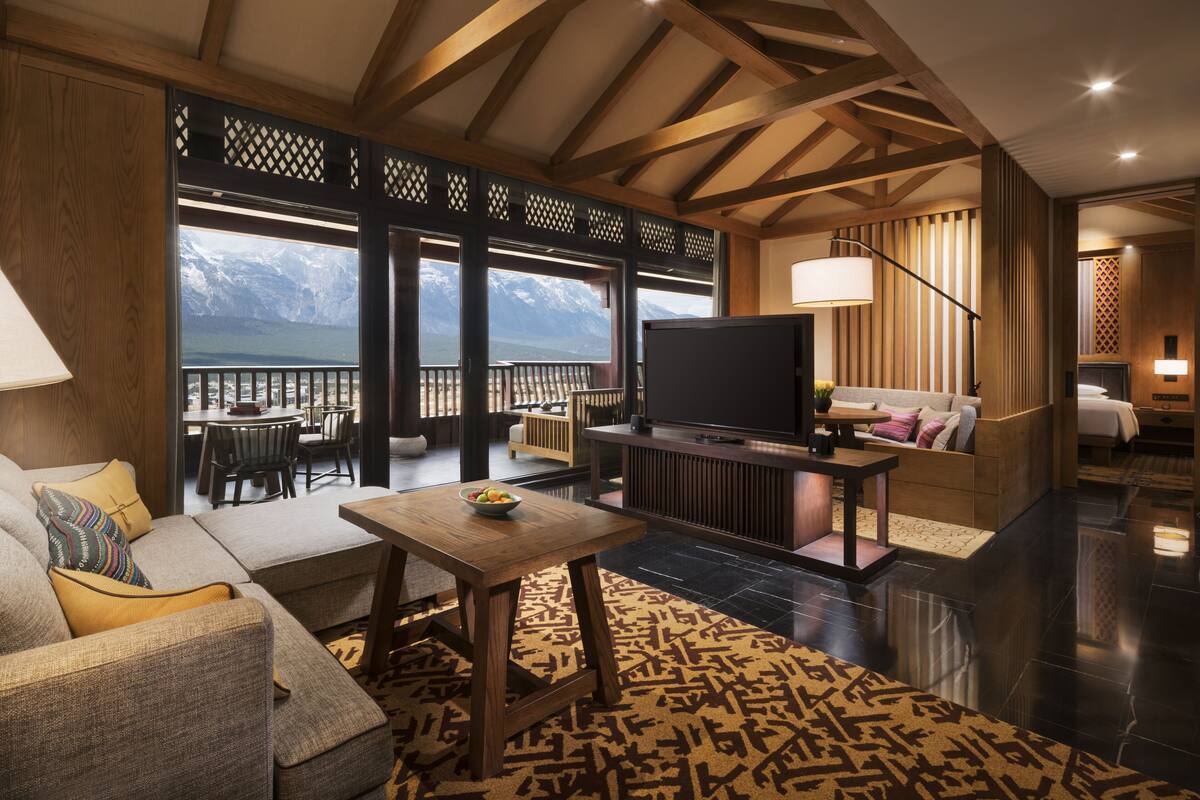 Una sala de estar moderna con sofá, mesa de centro y televisor. Cuenta con un ventanal con vistas a la montaña y un balcón.