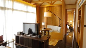 Ein modernes Hotelzimmer mit Holzboden, Flachbildfernseher, einer Couch, einer Lampe und Blick auf den Flur.