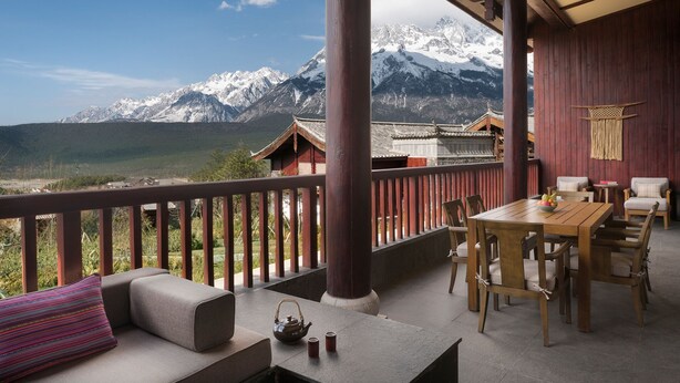 Ein Holzbalkon mit Tisch, Stühlen und einer Sitzecke, mit Blick auf schneebedeckte Berge.