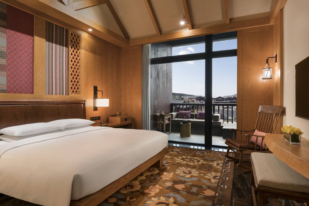 Habitación de hotel con una cama grande, un escritorio, una silla y vistas al exterior.