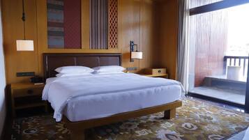 A hotel room with a large bed, a nightstand, a lamp, and a view of the outside.