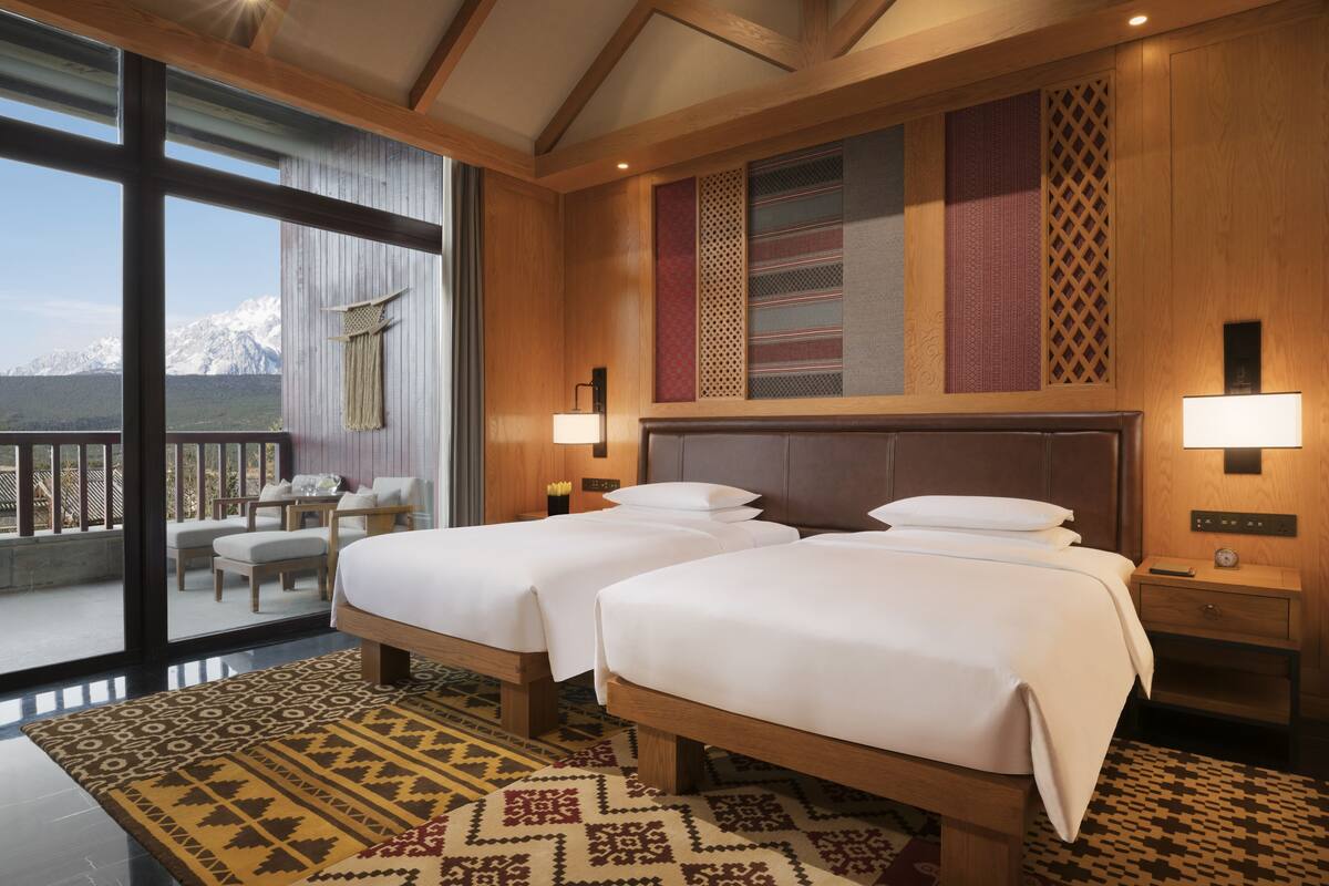 Habitación de hotel con dos camas, un balcón con vistas a montañas y una alfombra estampada.