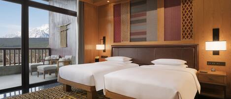 A hotel room with two beds, a balcony with a view of mountains, and a patterned rug.