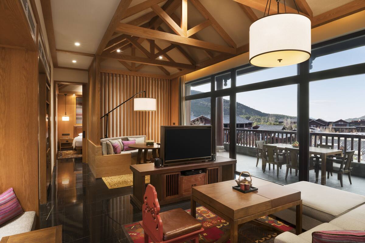 Amplia sala de estar con televisor grande, muebles de madera y un balcón con mobiliario exterior.
