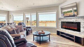 Uma sala de estar moderna com lareira, sofá de couro e grandes janelas com vista para um deck.