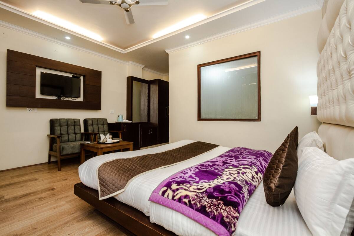 Quarto de hotel com uma cama, televisão na parede, escrivaninha e uma cadeira.