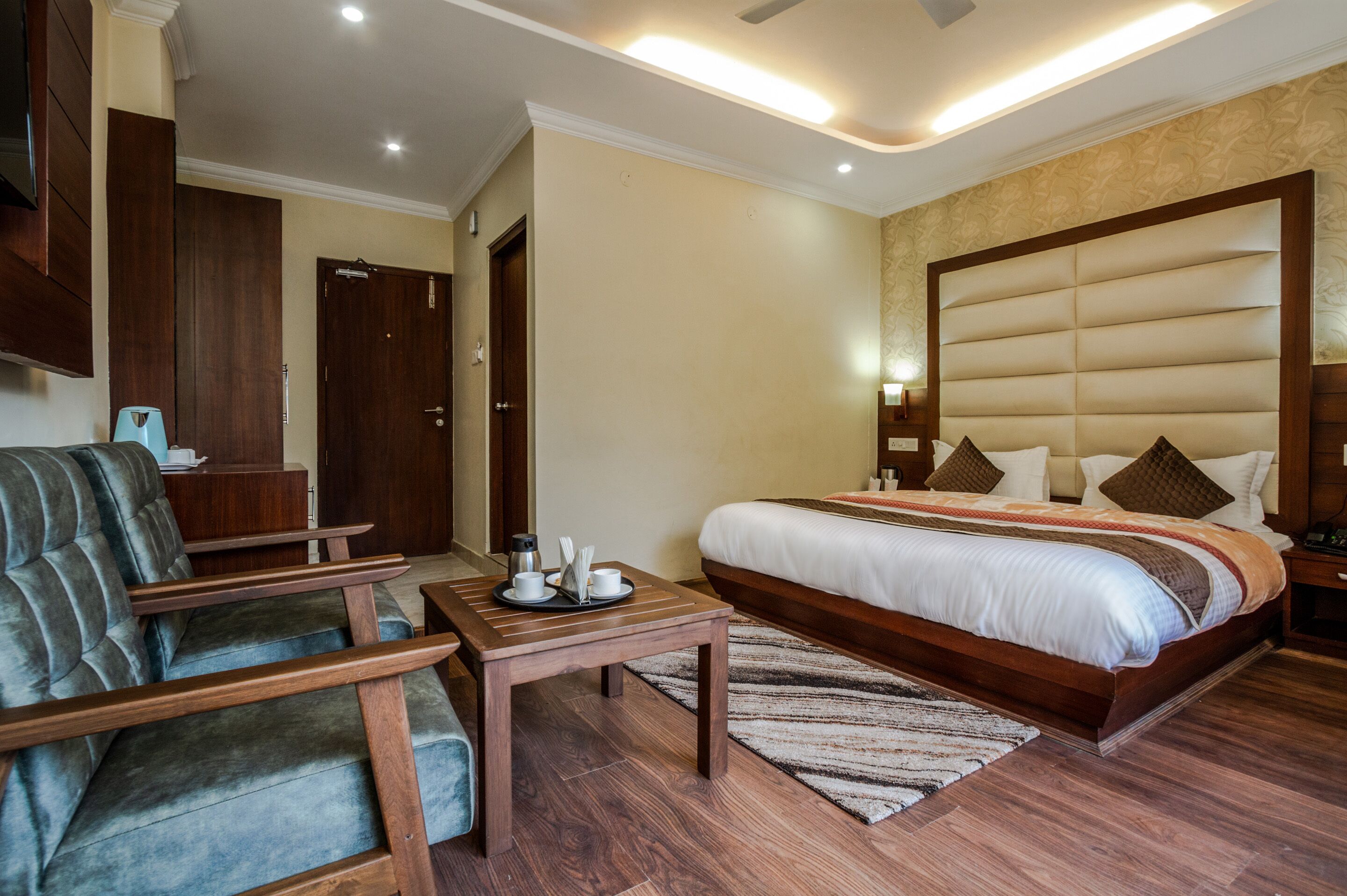 A hotel room with a large bed, a wooden nightstand, a desk with a chair, and a wardrobe.