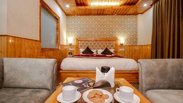 A hotel room with a wooden ceiling, a bed with a tufted headboard, two armchairs, a table with a plate of cookies, two cups, and a menu.