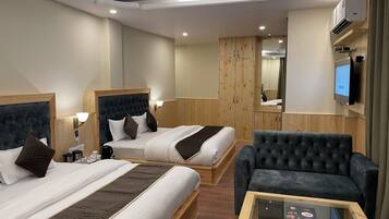Habitación de hotel con dos camas, un sillón gris, una mesita, armario de madera y televisor montado en la pared.