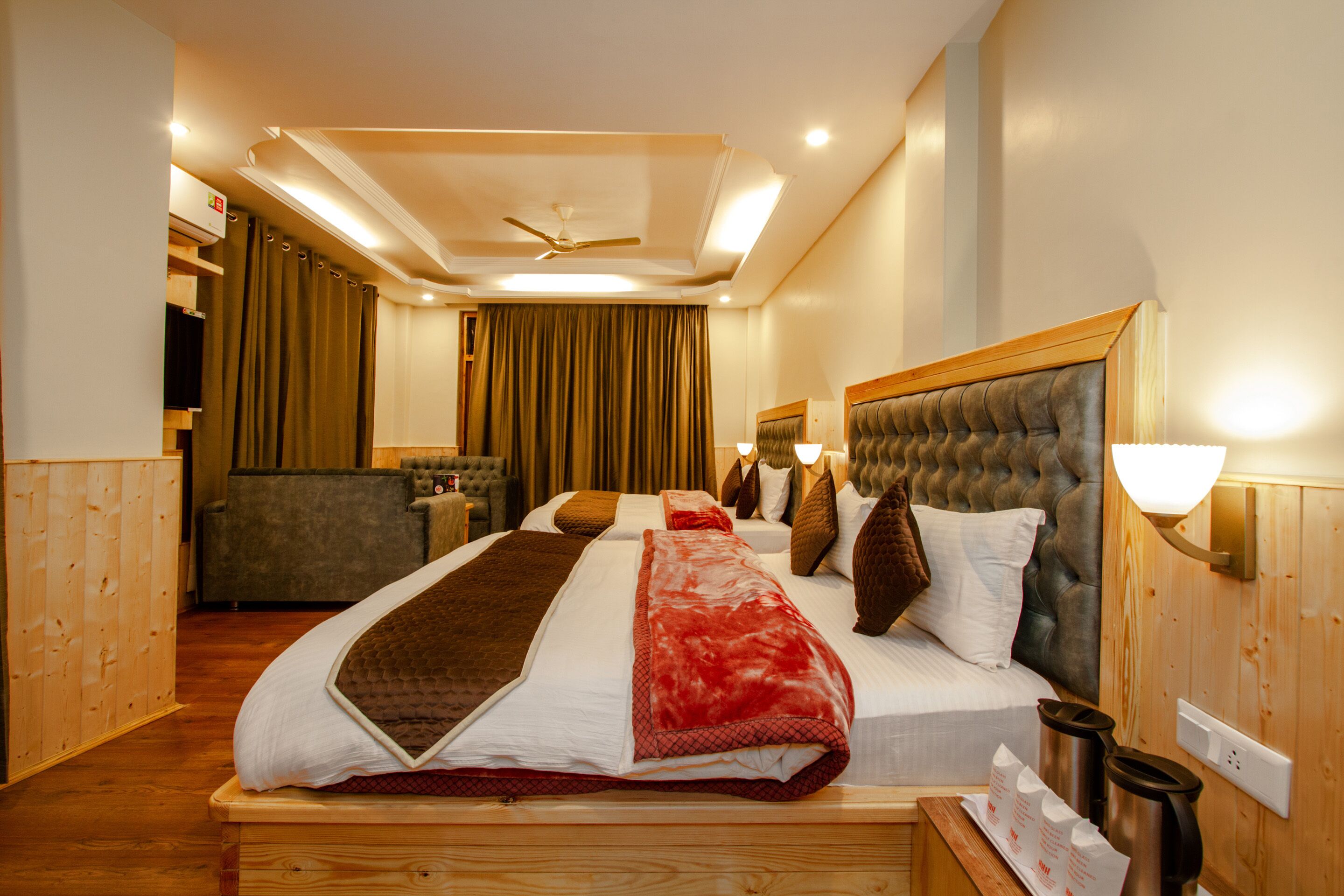 A hotel room with a large bed, a wooden headboard, a ceiling fan, and a seating area with a couch and curtains.