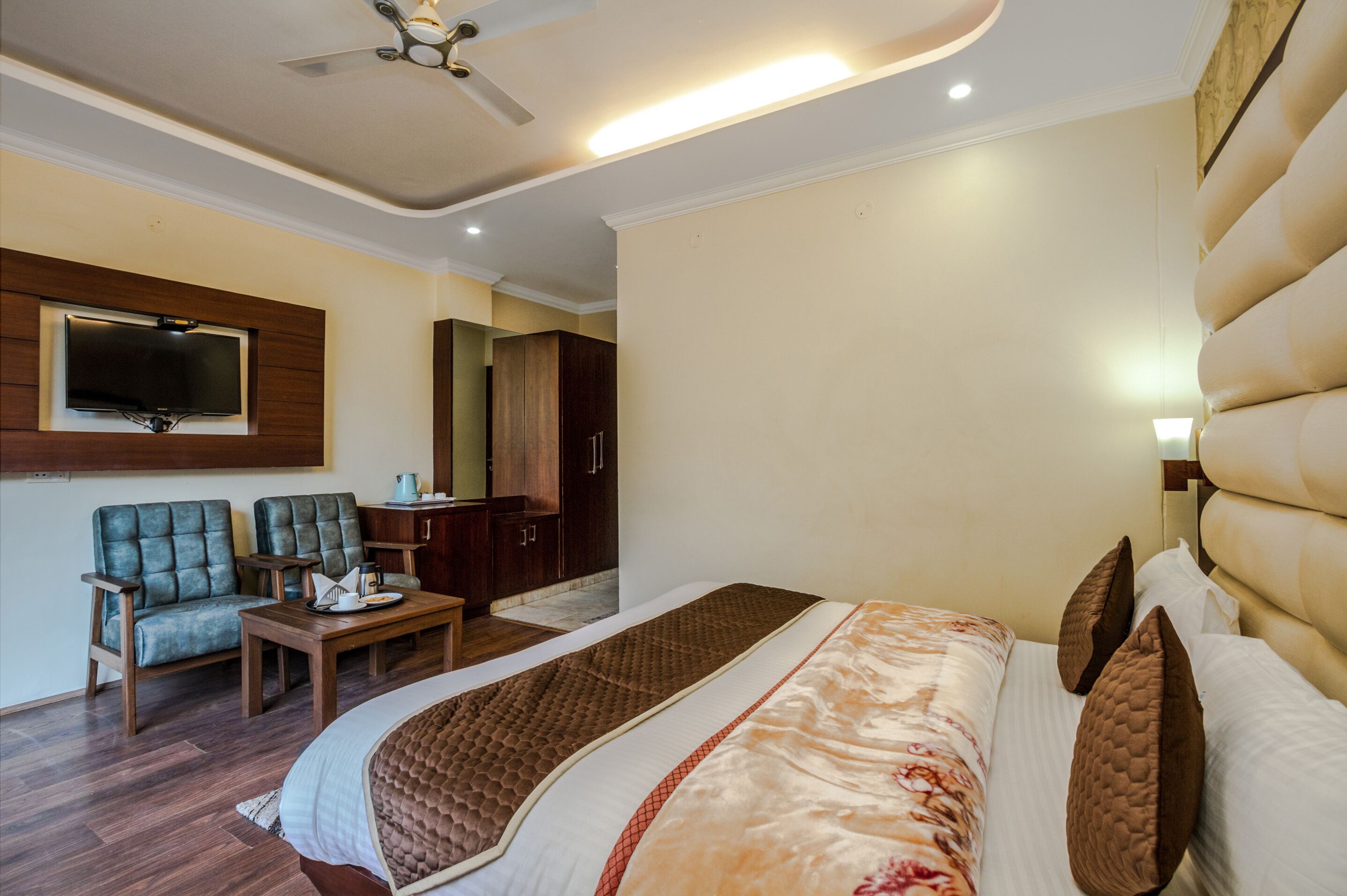 A hotel room with a large bed, a television mounted on the wall, a desk, and a seating area with chairs.