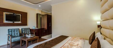 A hotel room with a large bed, a television mounted on the wall, a desk, and a seating area with chairs.