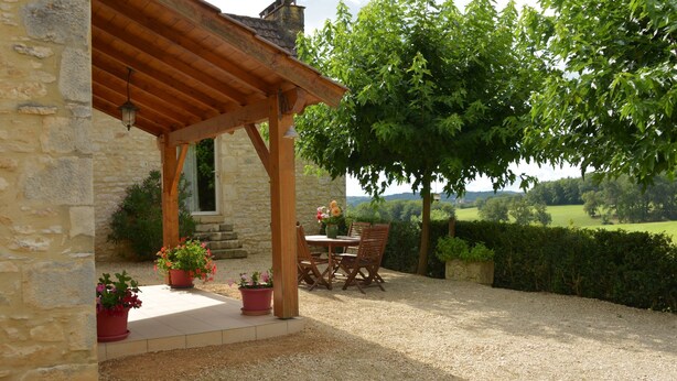Un bâtiment en pierre agrémenté d’une pergola en bois, avec des espaces de repos en plein air et des plantes en pot.