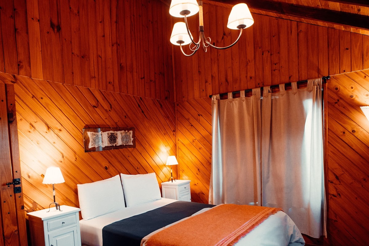 Een slaapkamer met houten lambrisering, een bed, nachtkastjes en een kroonluchter.