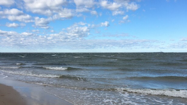 A beach with waves, a pier in the distance, and a clear sky.