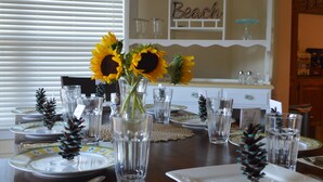 A dining table set with plates, cutlery, and clear glasses, with a vase of sunflowers in the center.