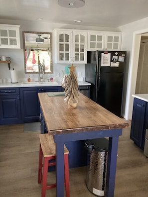 A kitchen with a wooden island, blue cabinets, a black refrigerator, and a small Christmas tree.
