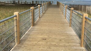A wooden boardwalk leading to the beach with metal railings on both sides.