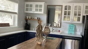 A kitchen with white cabinets, a wooden island, a stainless steel dishwasher, and a hanging light fixture.
