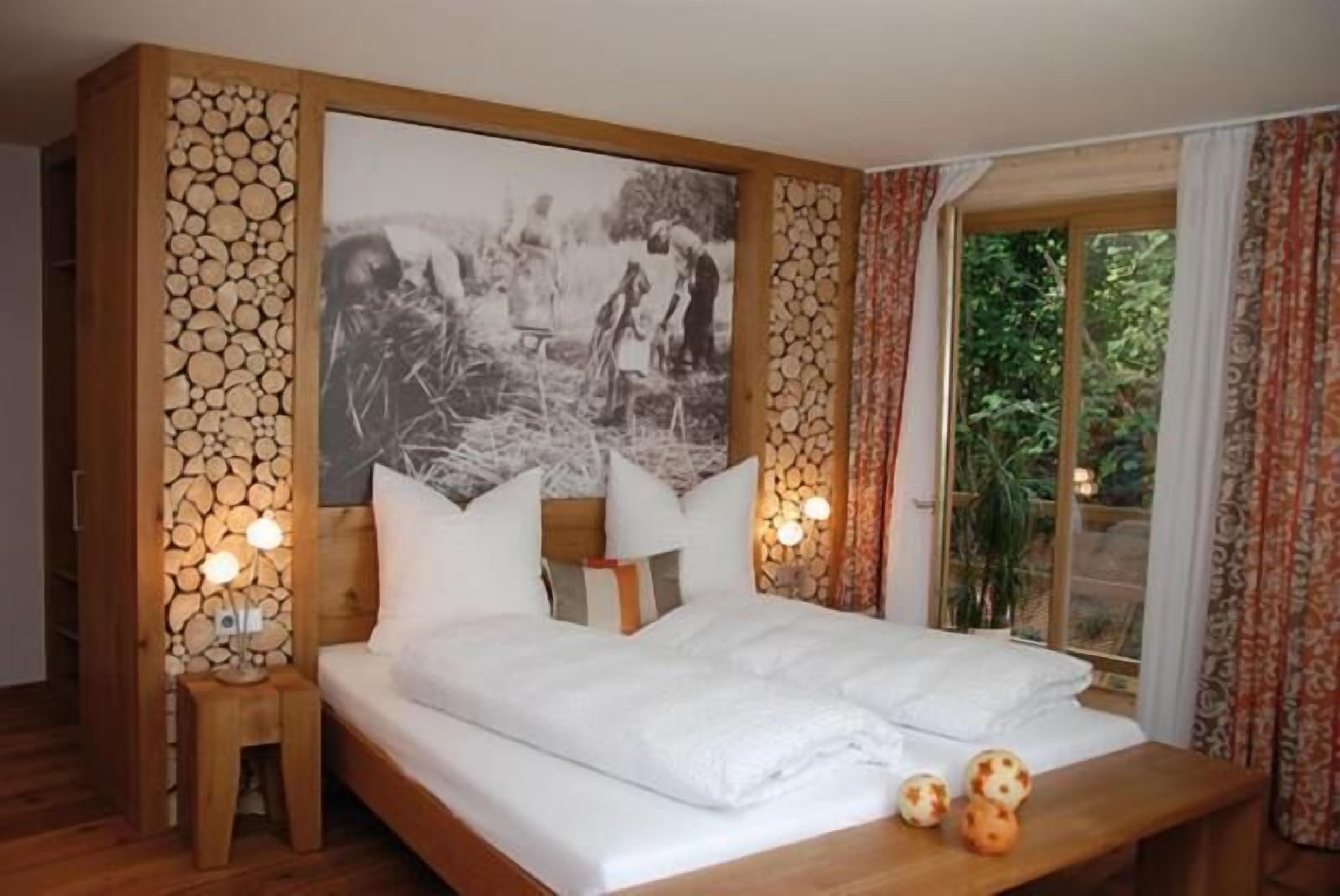 Ein Schlafzimmer mit einem großen Bett, zwei Nachttischen mit Lampen, einem hölzernen Kopfteil, einem Wandbild und einem Fenster mit Vorhängen.