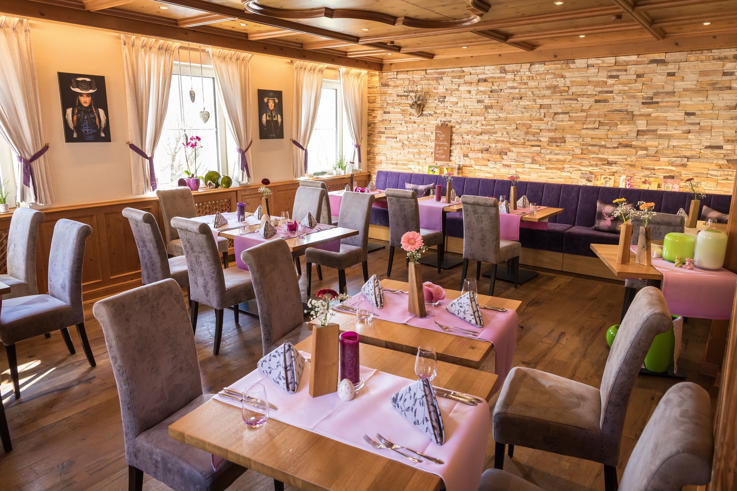 A restaurant with wooden tables and chairs, stone walls, and purple upholstered seating.