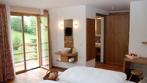Un dormitorio con una cama grande, un armario de madera, un baño con espejo y lavabo, y un ventanal corredero a un jardín.