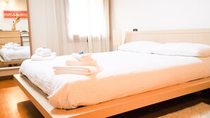 Un lit bien fait, avec du linge de lit et des serviettes blanches, une tête de lit en bois et une table de chevet en bois avec une lampe.
