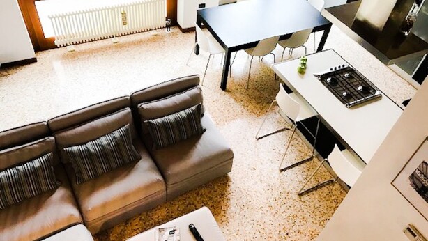 Une cuisine moderne avec une table à manger et des chaises, un canapé avec des coussins et une petite table sur laquelle se trouvent une télécommande et un magazine.