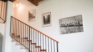 Un escalier avec des marches en bois et des rampes en métal noir, menant à un palier où sont accrochées trois photographies encadrées au mur.