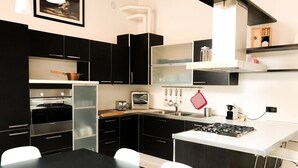 Une cuisine moderne avec des meubles noirs, un plan de travail blanc et une cuisinière. On y trouve une table à manger avec un saladier rempli de pommes.