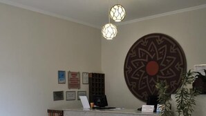A reception area with a marble counter, a decorative wall piece, a potted plant, and a round wooden table. - Hotel Oriente (Itajuba)