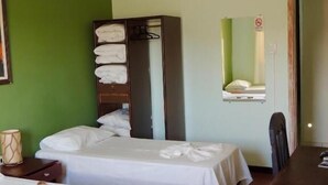A hotel room with two beds, a wardrobe, a dining table, and a ceiling fan. - Hotel Oriente (Itajuba)