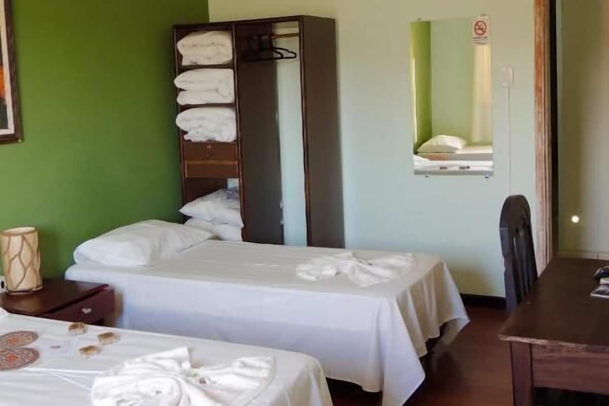 Habitación de hotel con dos camas, un armario, una mesa de comedor y un ventilador de techo.