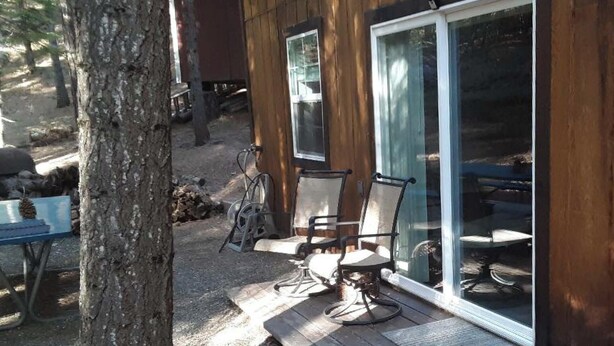 Une terrasse en bois, dotée de mobilier d’extérieur, notamment des chaises et une table, ainsi qu’une grande porte-fenêtre coulissante.