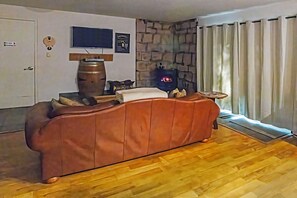 A living room with a brown sofa, a television mounted on the wall, a stone wall, and a window with curtains. - Winterfell - No Hidden Fee; Dog OK; King Bed (Arnold)