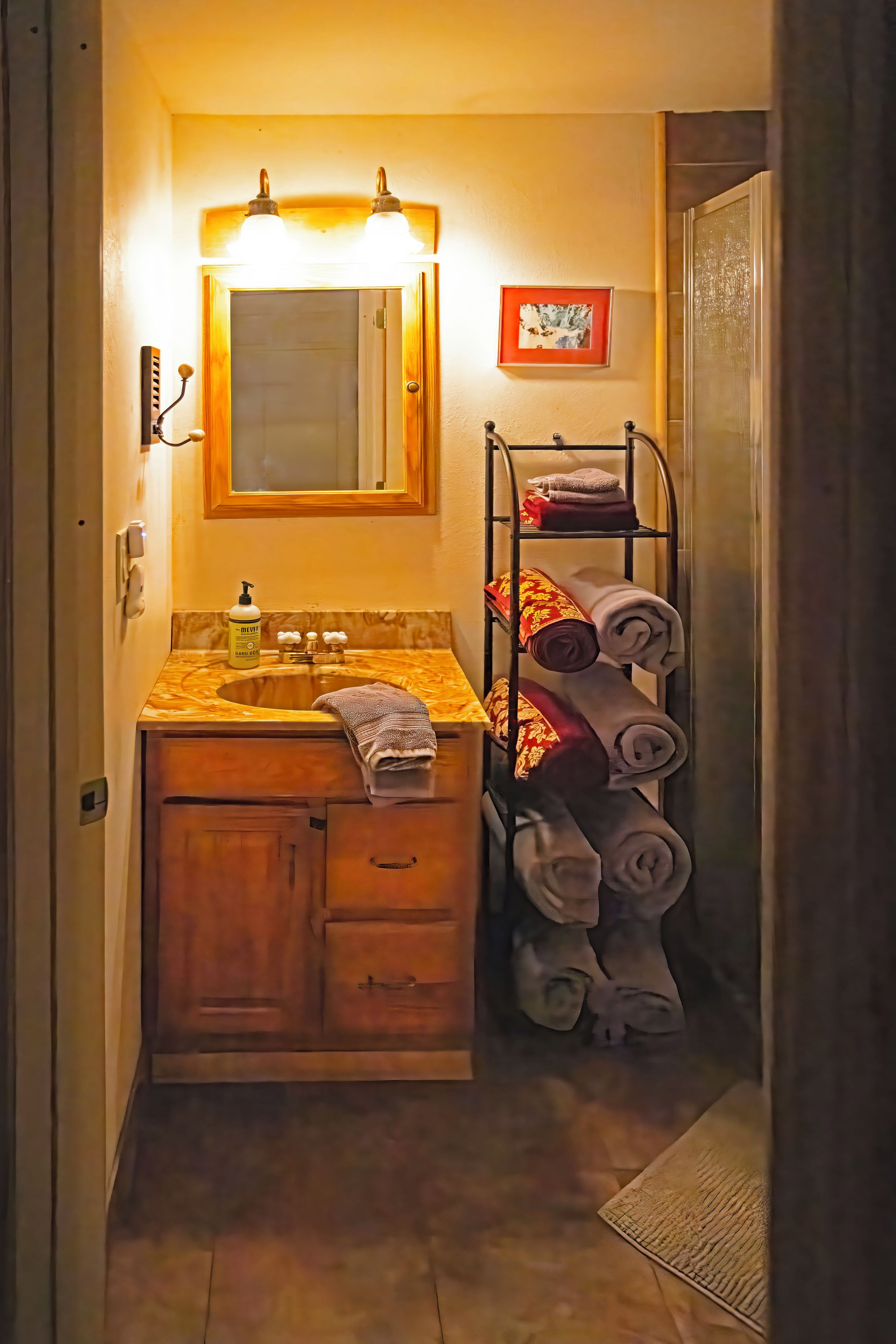 A bathroom with a wooden vanity, a mirror, a towel rack with towels, and a framed picture on the wall.