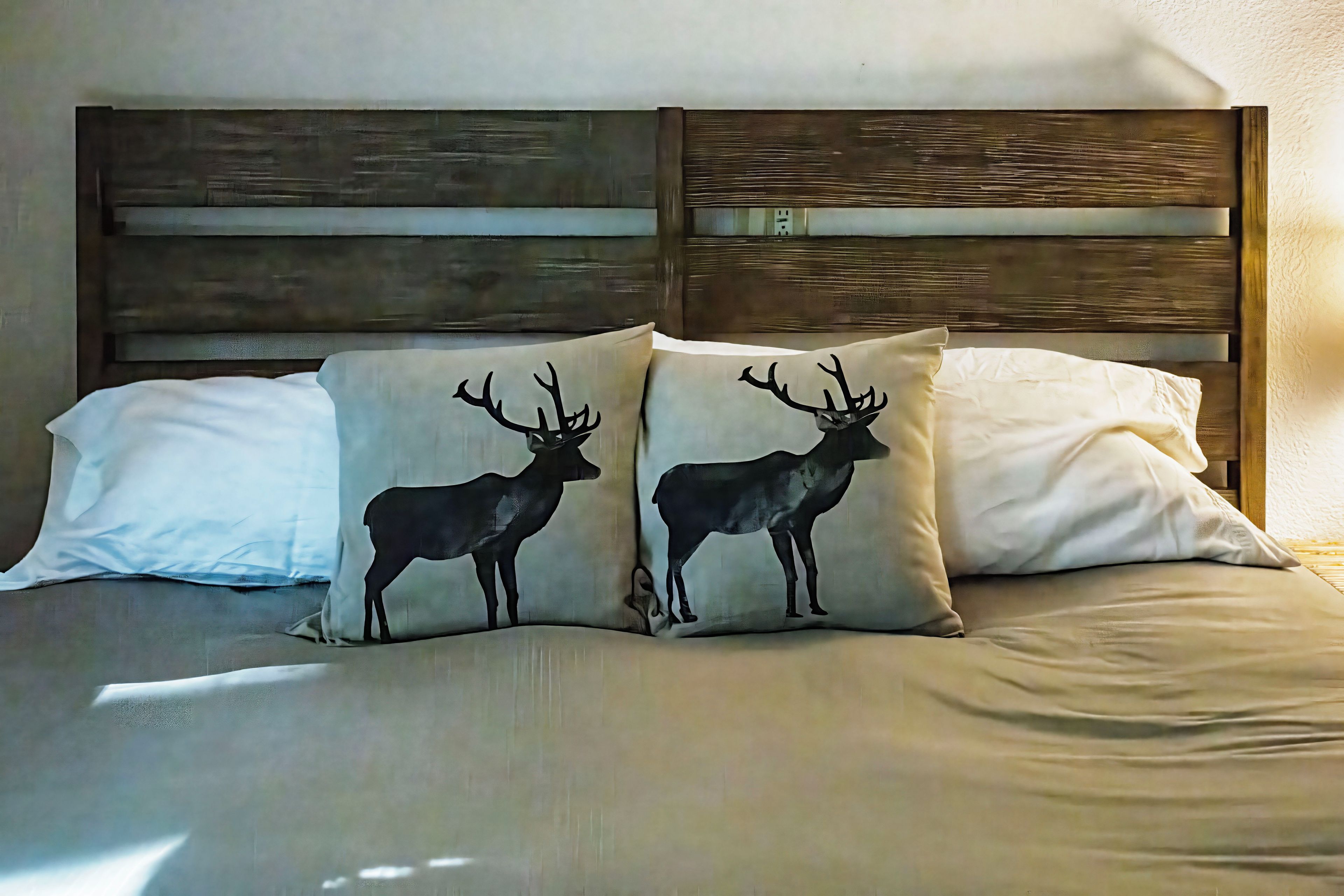 A bed with a wooden headboard and two pillows with deer designs.