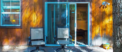 A wooden cabin with a sliding glass door, two chairs, and a small table.