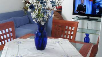 A living room with a blue vase on a table, a blue sofa, and a television on a stand.