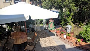 An outdoor patio area with a round wooden table and chairs, a white umbrella, and potted plants. - Residence le Rose (Bibbona)