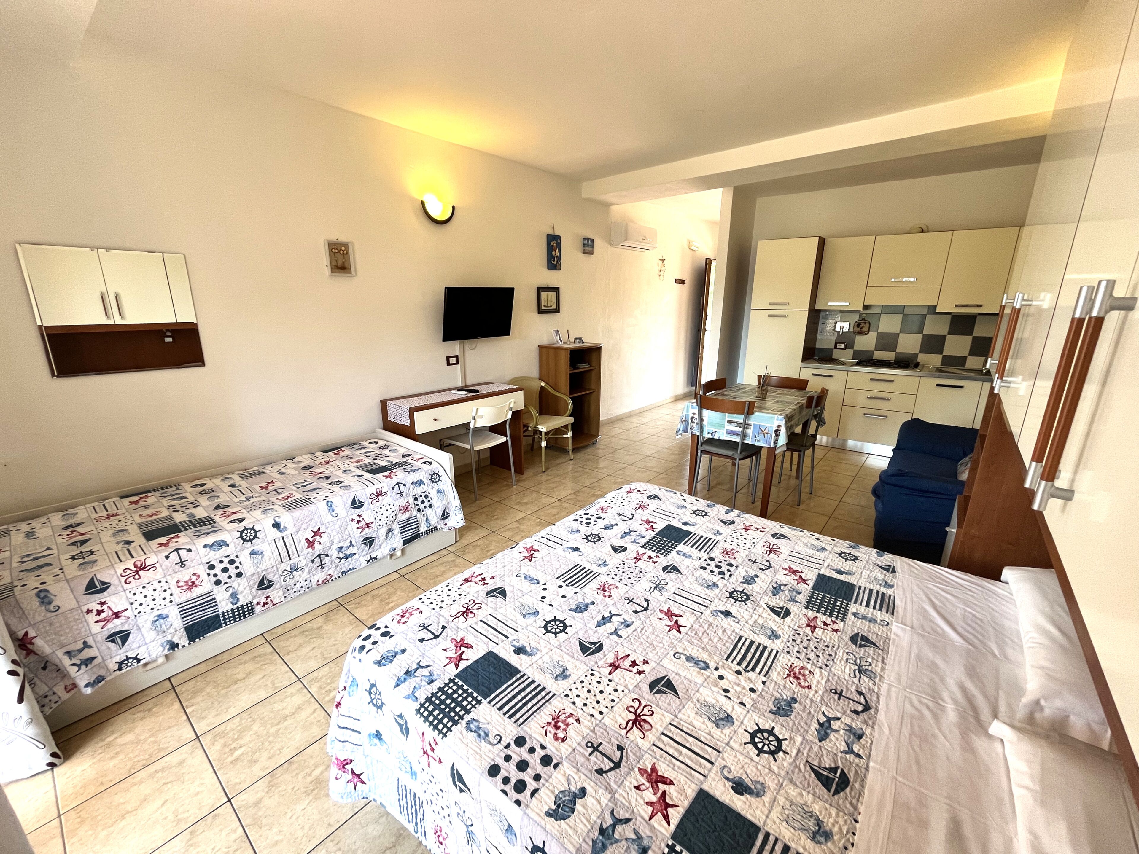 Une chambre d’hôtel avec deux lits, un bureau, une chaise, une télévision et une kitchenette.