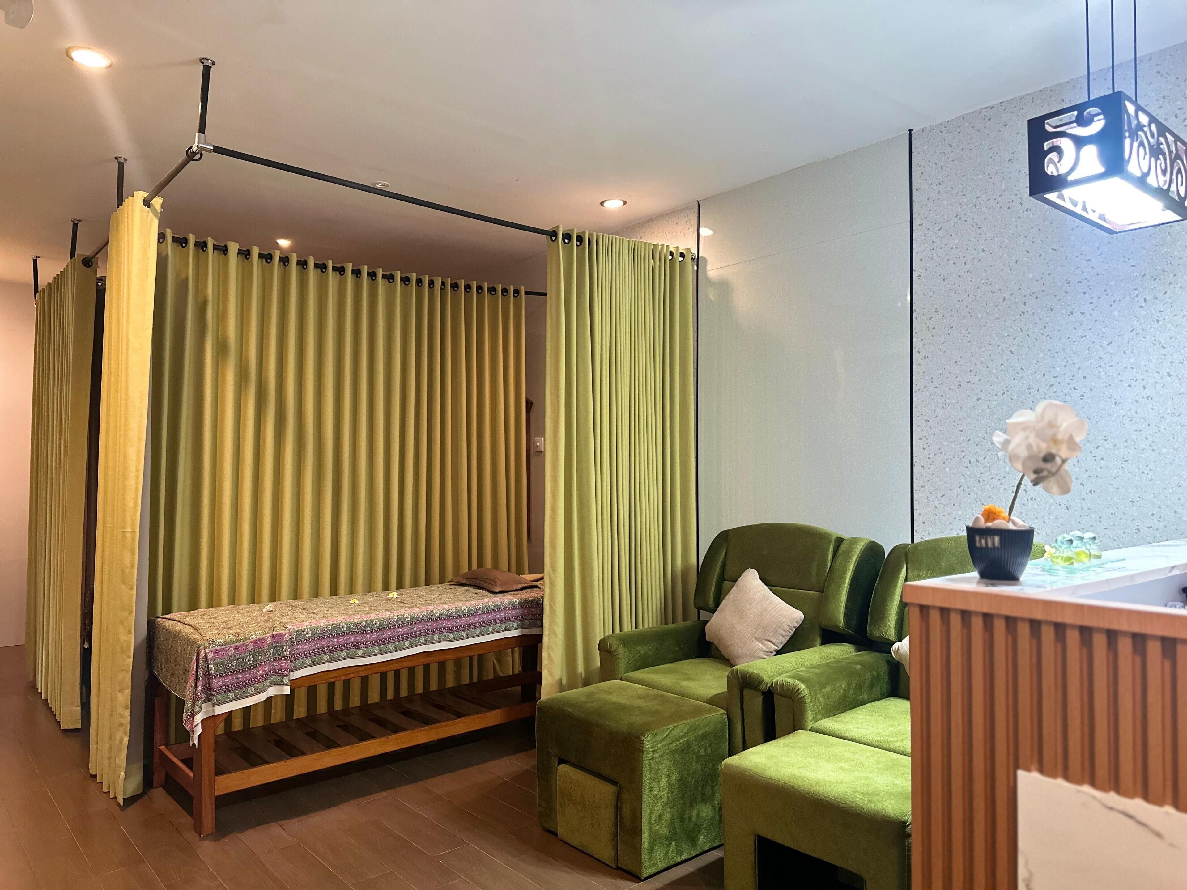Una habitación con una cama, un sofá verde, una mesita con un cuenco y flores, y una lámpara colgante.