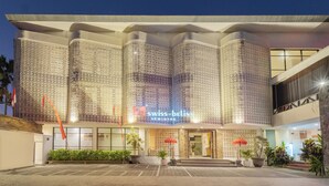 A modern hotel with a distinctive facade featuring intricate lattice patterns, a prominent entrance with steps, and potted plants at the entrance. - Swiss-Belinn Seminyak (Denpasar)