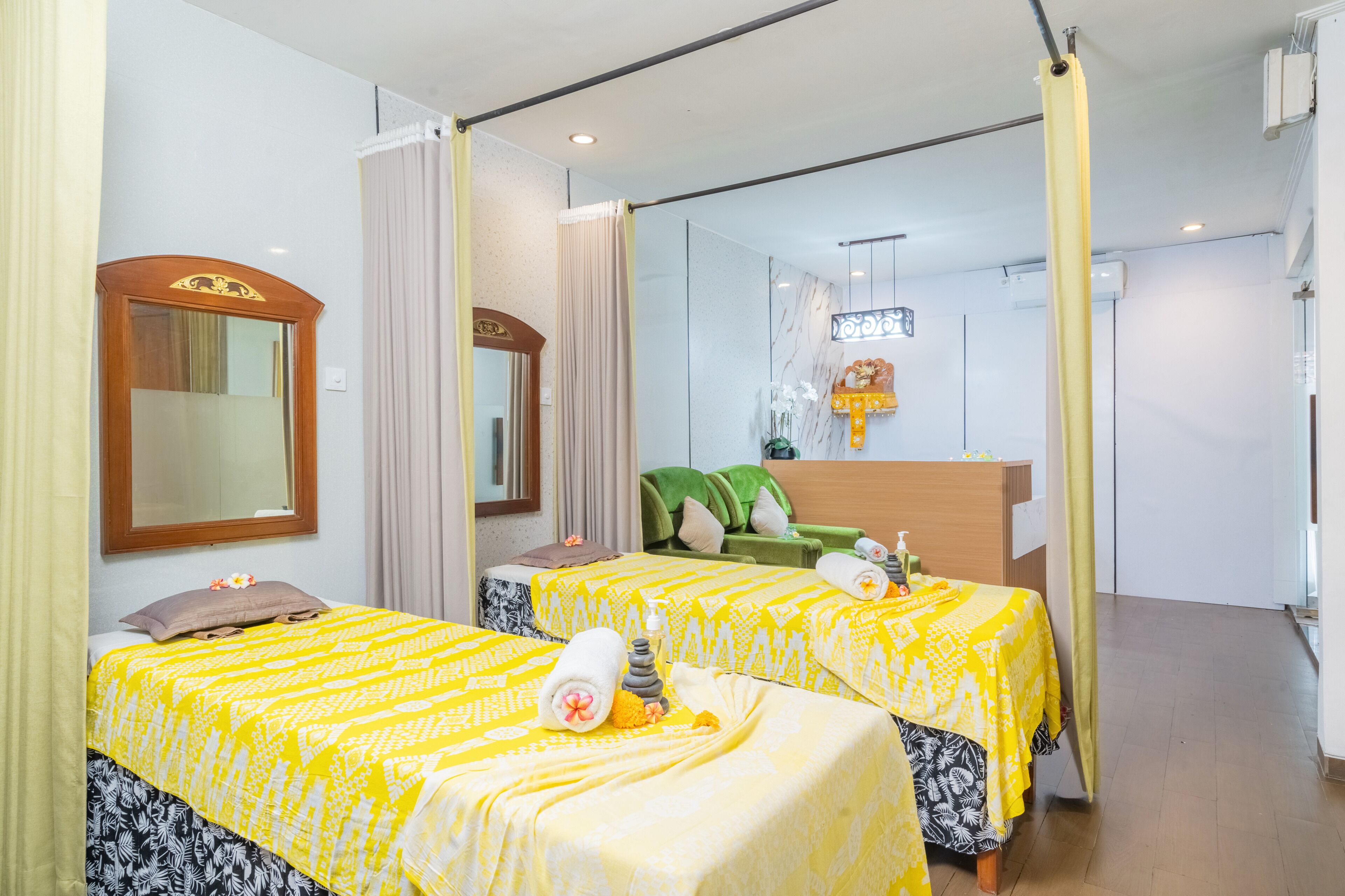 A hotel room with two beds, a mirror, a green chair, and a small table with a lamp.