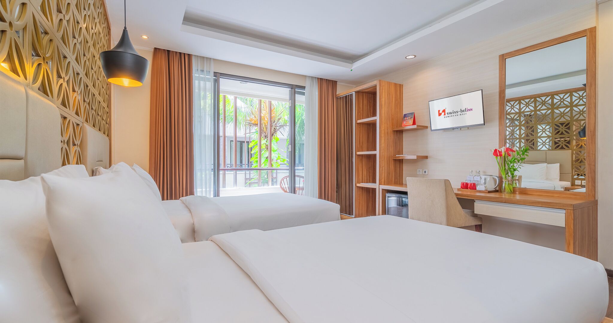 A hotel room with two beds, a desk, a mirror, and a TV.