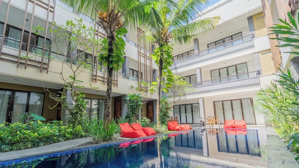 A modern hotel with a pool, red lounge chairs, and lush greenery. - Swiss-Belinn Seminyak (Denpasar)