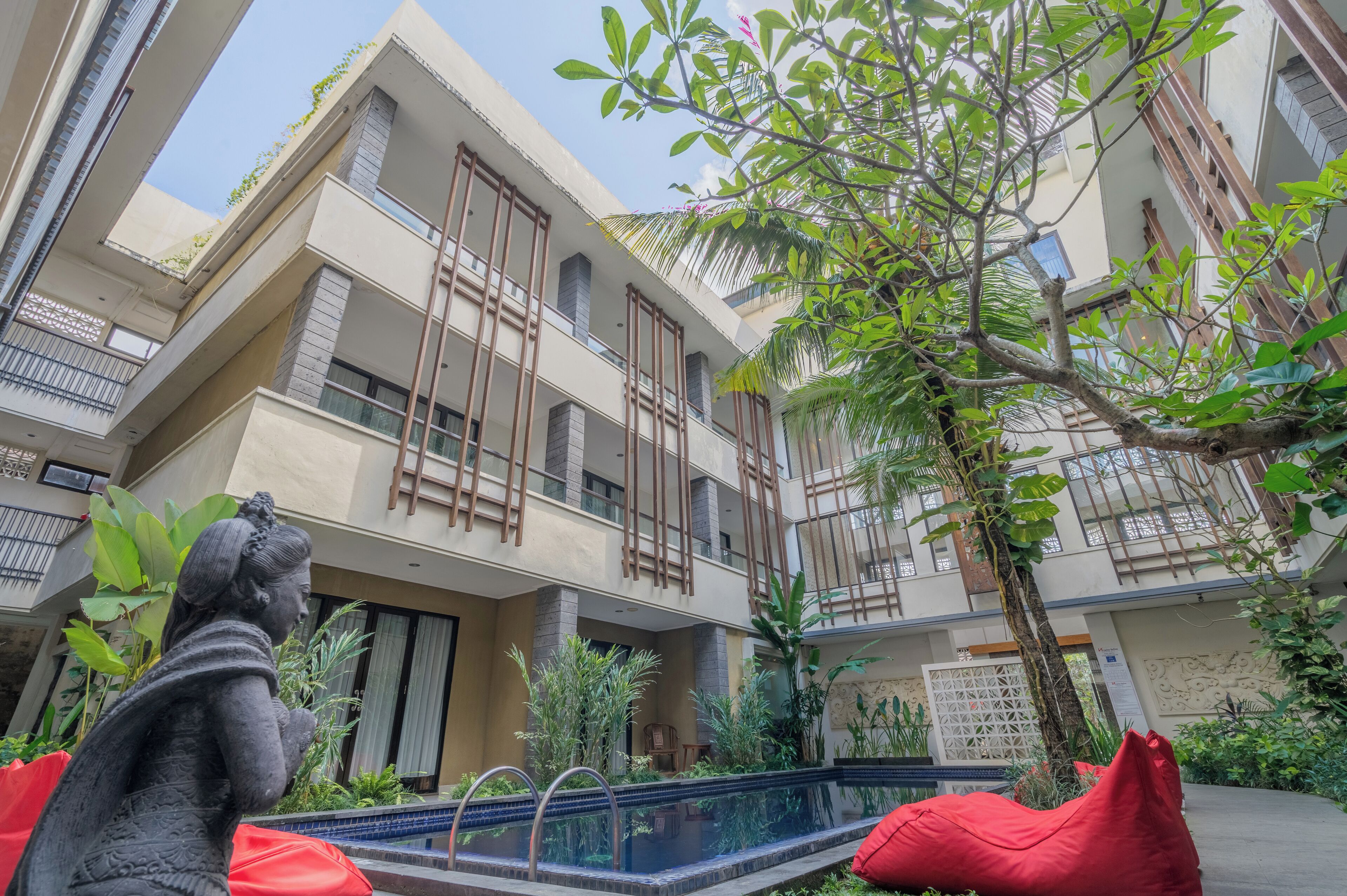 A multi-story building with balconies, a swimming pool, and lush greenery.