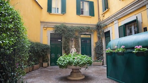 A courtyard with a large planter, a statue, and a building with green shutters. - IMHOME - Cadorna House (Milan)